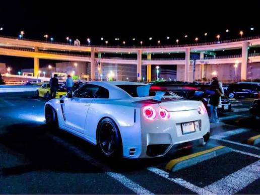 Weißer Nissan GT-R R35 mit Aftermarket-Heckflügel nachts an der Daikoku PA